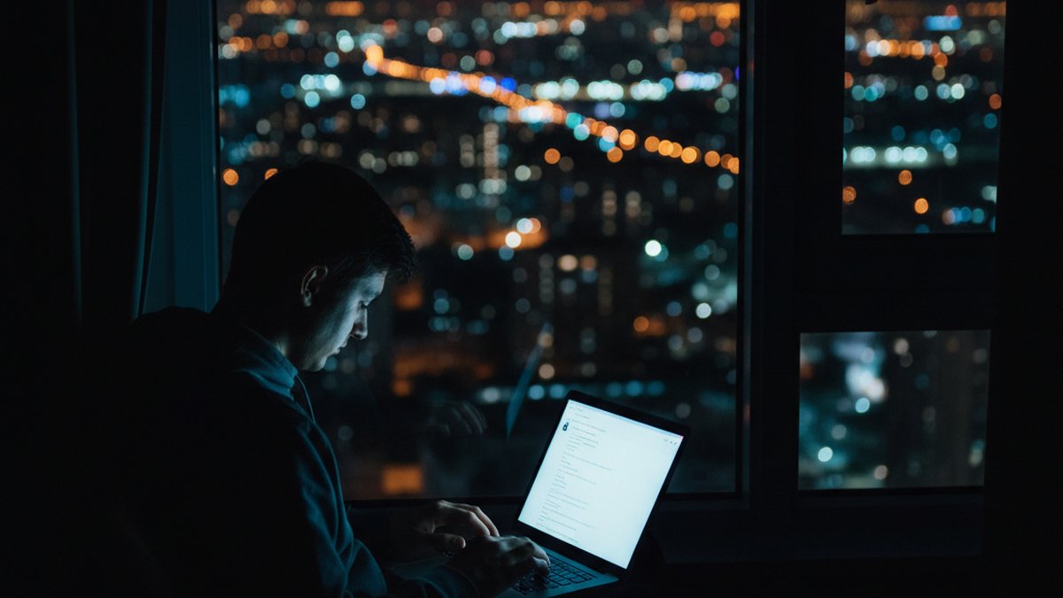 Silhouette of a person scrolling social media by a window at night