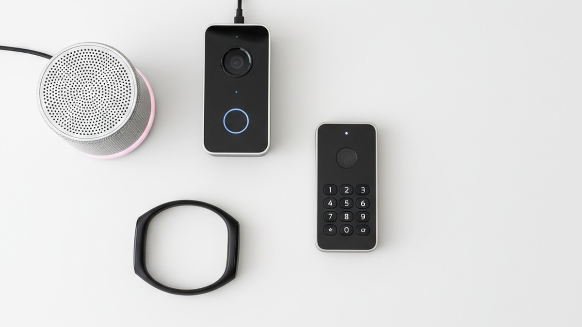 Flat-lay of smart home devices including smart speaker, doorbell camera, and fitness tracker arranged on white desk
